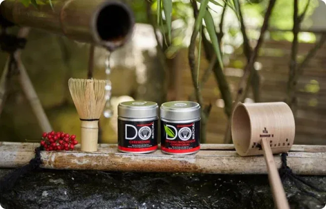 DōMatcha tins and tea tools near a bamboo water feature